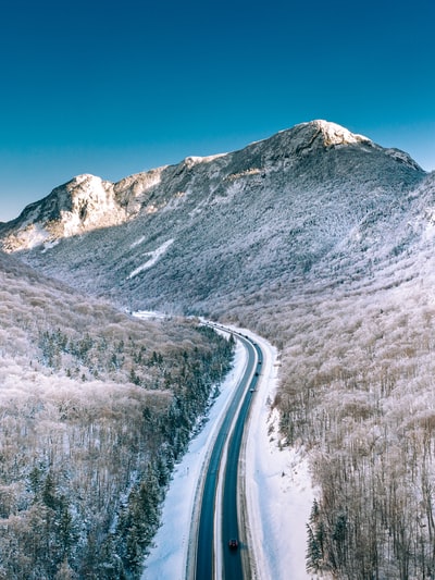 被雪覆盖的道路附近的山在蓝天白天
